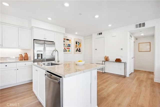 kitchen featuring light stone counters, an island with sink, white cabinets, and appliances with stainless steel finishes