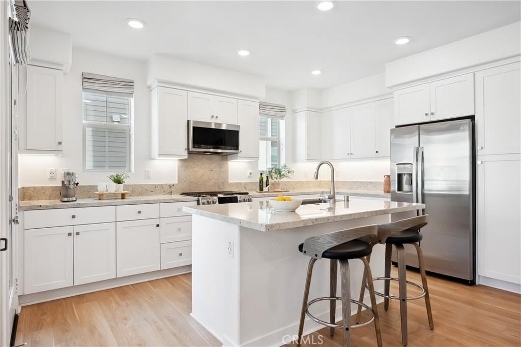 kitchen with sink, light hardwood / wood-style flooring, a center island with sink, appliances with stainless steel finishes, and white cabinets