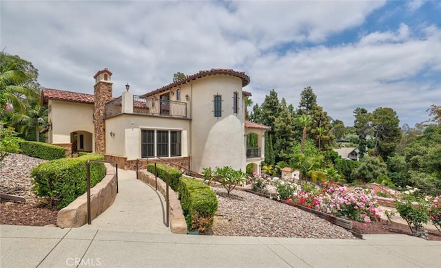 exterior space featuring a tiled roof, stone siding, a chimney, a balcony, and stucco siding