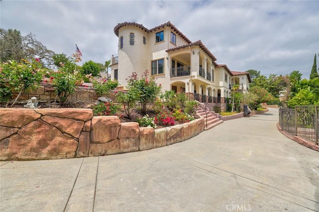 view of side of property with stucco siding, a tile roof, a balcony, and fence