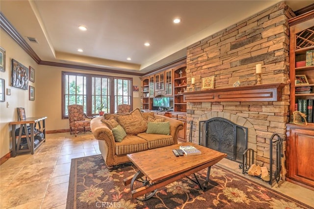 living room with built in features, a stone fireplace, and a tray ceiling