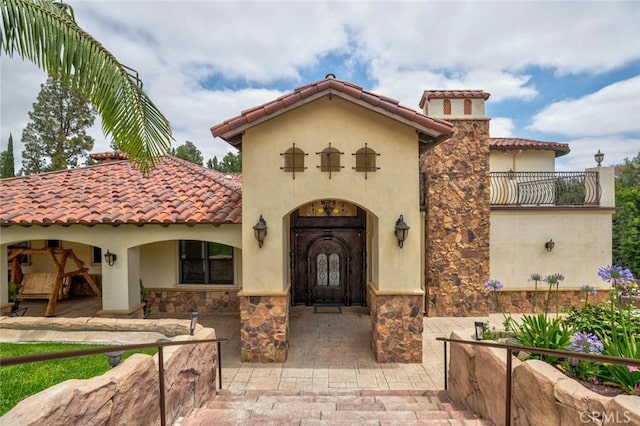 property entrance with stone siding, a tiled roof, and stucco siding