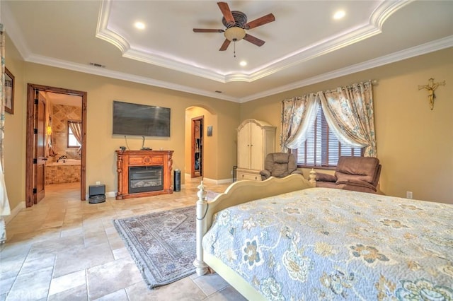 bedroom with ceiling fan, ornamental molding, connected bathroom, and a raised ceiling