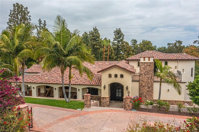 mediterranean / spanish home with a tile roof, a balcony, and stucco siding