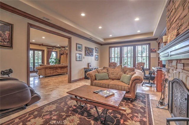 living room with visible vents, recessed lighting, crown molding, a stone fireplace, and a raised ceiling