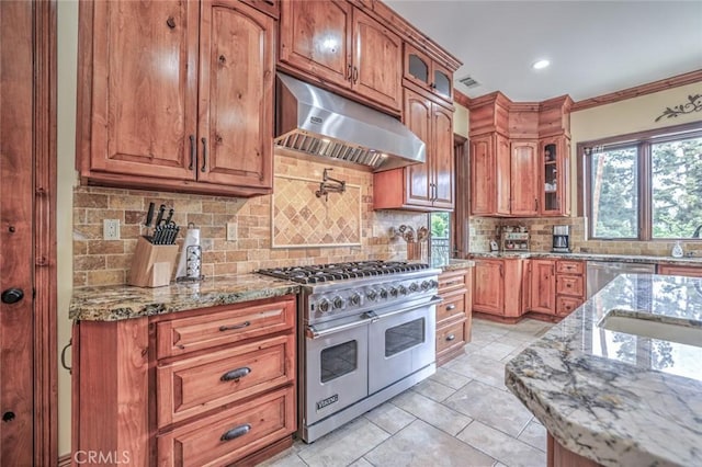 kitchen featuring backsplash, glass insert cabinets, light stone countertops, under cabinet range hood, and appliances with stainless steel finishes