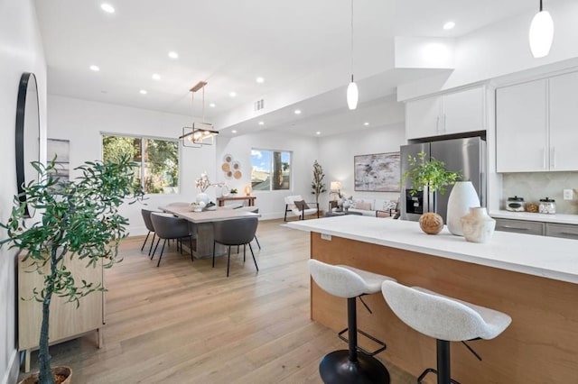 kitchen with white cabinetry, backsplash, hanging light fixtures, light hardwood / wood-style floors, and stainless steel fridge with ice dispenser