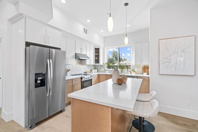 kitchen with appliances with stainless steel finishes, hanging light fixtures, backsplash, white cabinets, and a kitchen island