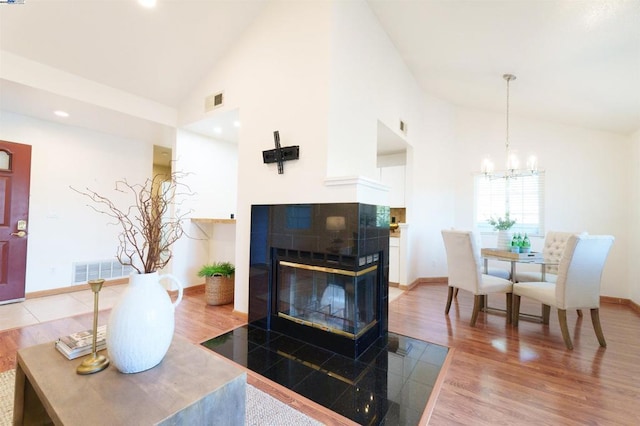 living room with hardwood / wood-style flooring, a fireplace, high vaulted ceiling, and a notable chandelier