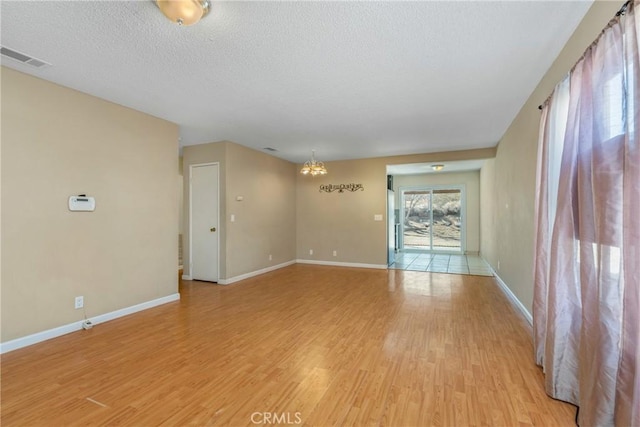 spare room with a chandelier, a textured ceiling, and light wood-type flooring