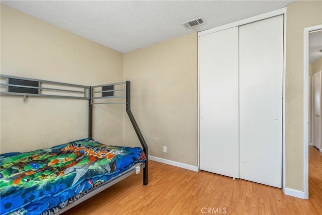 bedroom with a closet, a textured ceiling, and light wood-type flooring