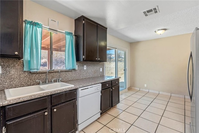 kitchen with light tile patterned flooring, stainless steel refrigerator, tasteful backsplash, dishwasher, and sink