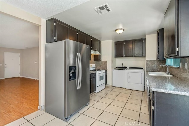 kitchen with sink, light tile patterned floors, washer and clothes dryer, stainless steel fridge, and white range with gas cooktop