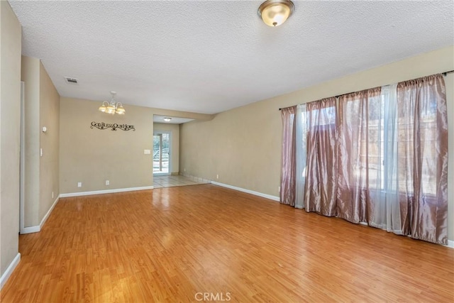 empty room with an inviting chandelier, hardwood / wood-style floors, and a textured ceiling