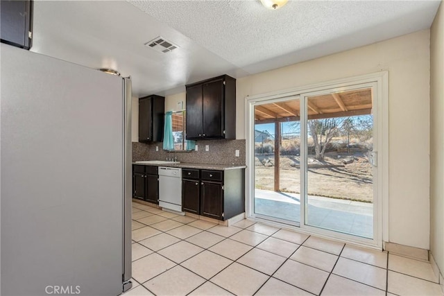 kitchen featuring a textured ceiling, light tile patterned floors, stainless steel refrigerator, white dishwasher, and decorative backsplash