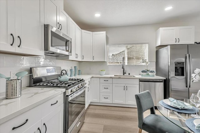 kitchen with sink, white cabinetry, appliances with stainless steel finishes, light stone countertops, and light hardwood / wood-style floors