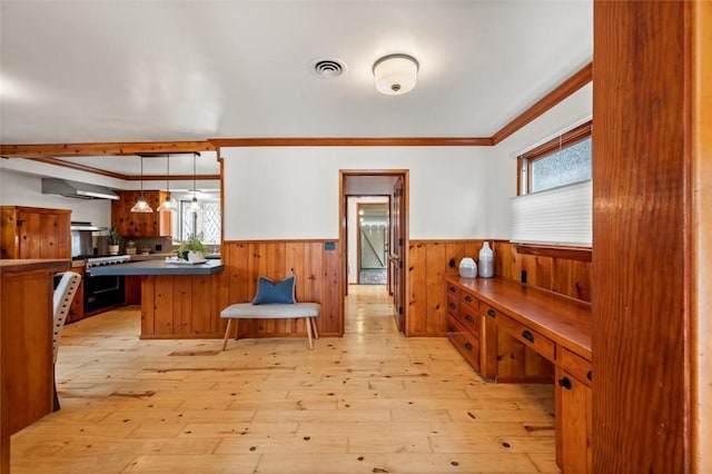 interior space featuring decorative light fixtures, light hardwood / wood-style floors, ornamental molding, kitchen peninsula, and beam ceiling