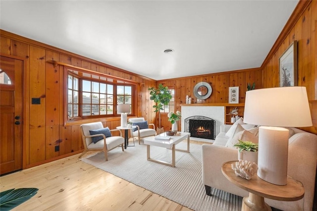 living room with wood walls, light hardwood / wood-style flooring, crown molding, and a fireplace