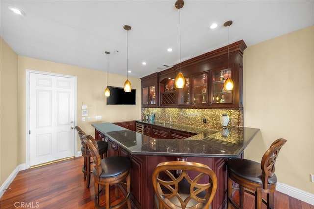 bar featuring tasteful backsplash, dark hardwood / wood-style floors, dark stone countertops, sink, and hanging light fixtures