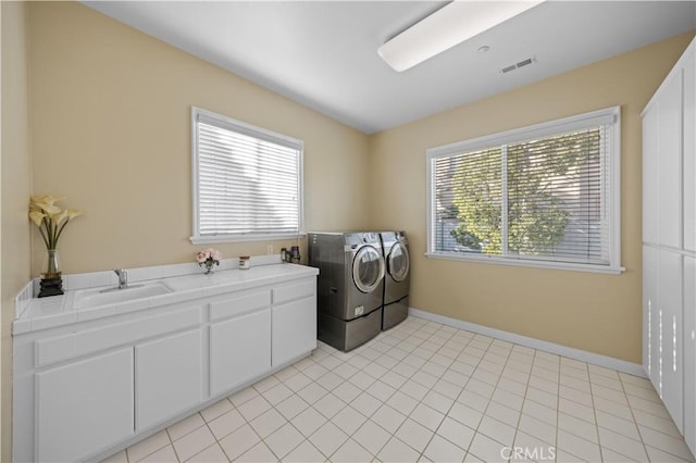 clothes washing area with cabinets, sink, washer and clothes dryer, and a healthy amount of sunlight