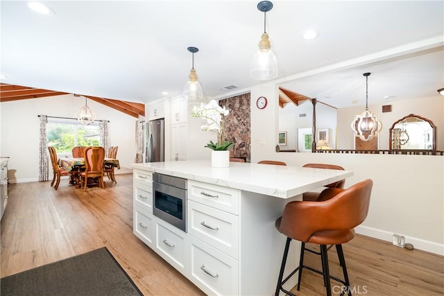 kitchen with white cabinets, appliances with stainless steel finishes, a kitchen island, hanging light fixtures, and lofted ceiling with beams