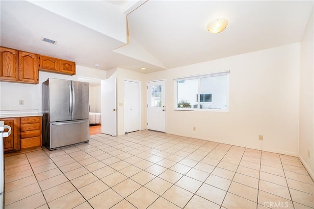 kitchen with light tile patterned floors, vaulted ceiling, and stainless steel fridge