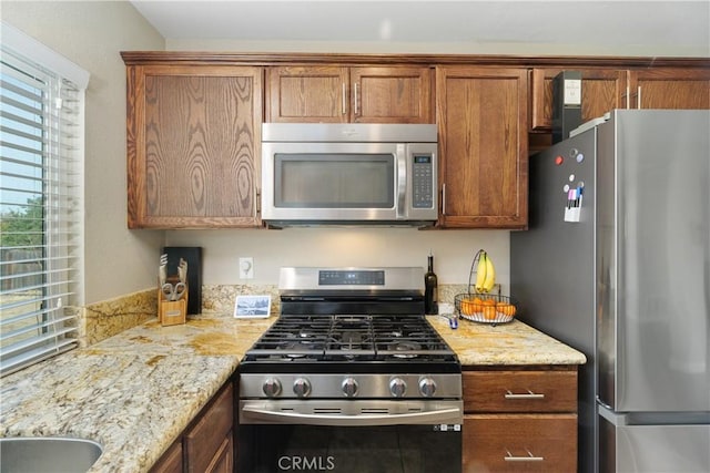 kitchen with stainless steel appliances, light stone countertops, and sink