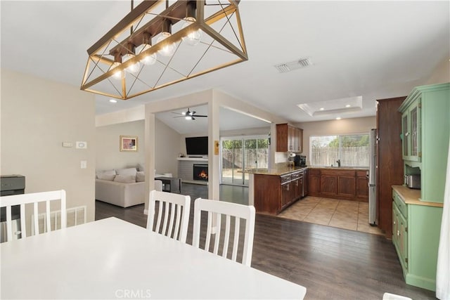 dining room featuring sink, vaulted ceiling, a tray ceiling, a fireplace, and hardwood / wood-style floors