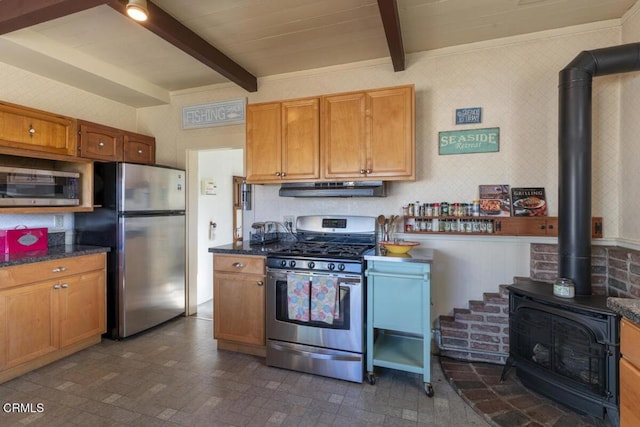 kitchen featuring under cabinet range hood, beam ceiling, a wood stove, and appliances with stainless steel finishes