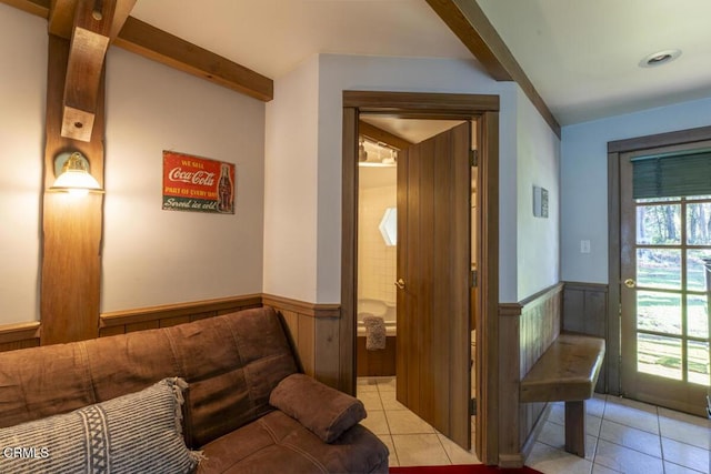 living area featuring light tile patterned flooring, beamed ceiling, and a wainscoted wall