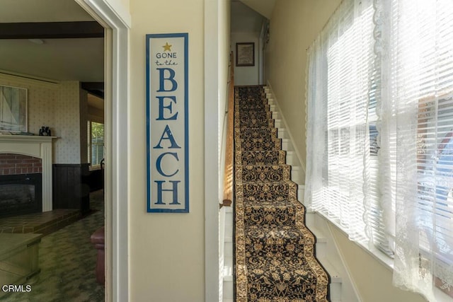 stairway with wallpapered walls, wainscoting, and a brick fireplace