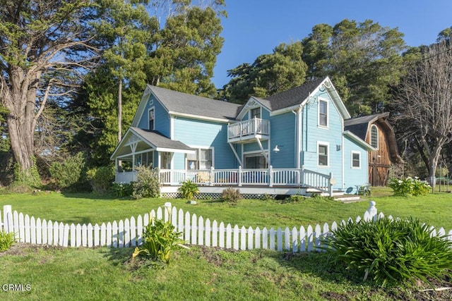 victorian house featuring a front yard, fence, and a balcony