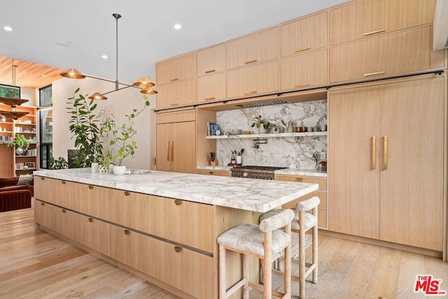 kitchen with a breakfast bar area, decorative backsplash, range, light brown cabinets, and light hardwood / wood-style flooring