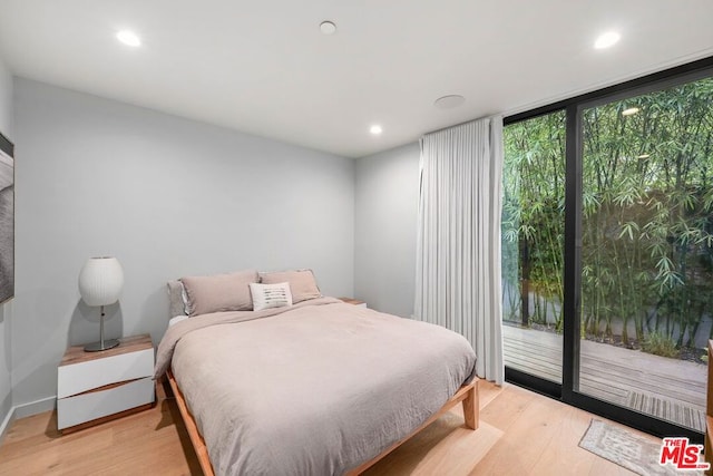 bedroom featuring access to exterior, light wood-type flooring, and a wall of windows