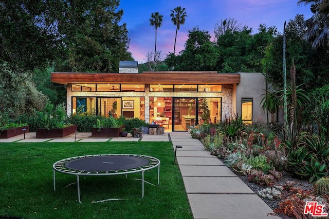 back house at dusk with a patio, a yard, and a trampoline