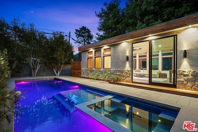 pool at dusk featuring an in ground hot tub and a patio