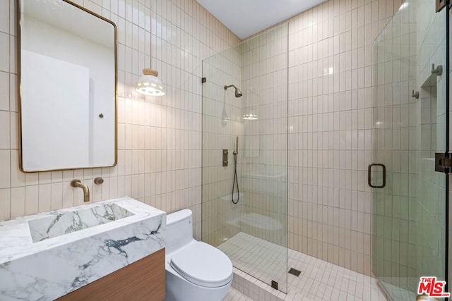 bathroom with vanity, toilet, a shower with door, and tile walls