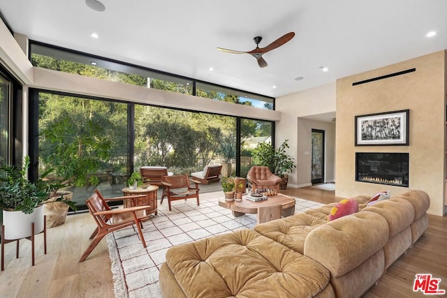 living room with ceiling fan, a large fireplace, floor to ceiling windows, and light hardwood / wood-style floors