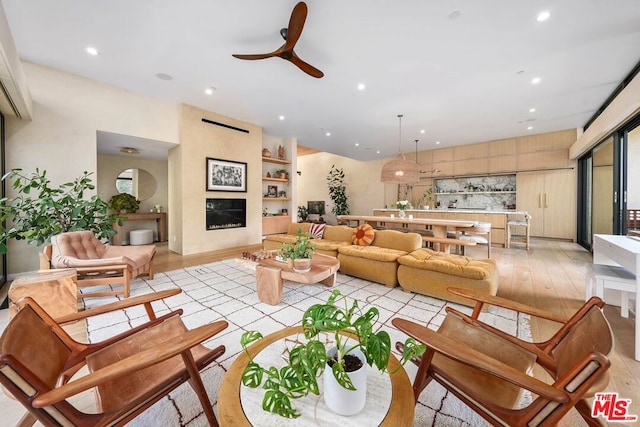 living room featuring light hardwood / wood-style flooring, a large fireplace, and ceiling fan