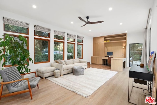 living room with ceiling fan, plenty of natural light, built in desk, and light wood-type flooring