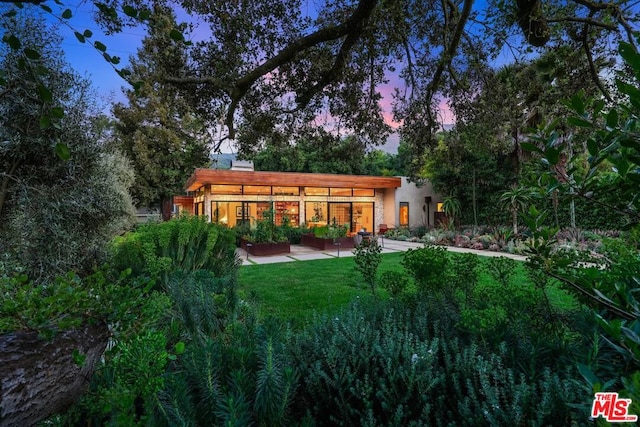 back house at dusk featuring a lawn and a patio area