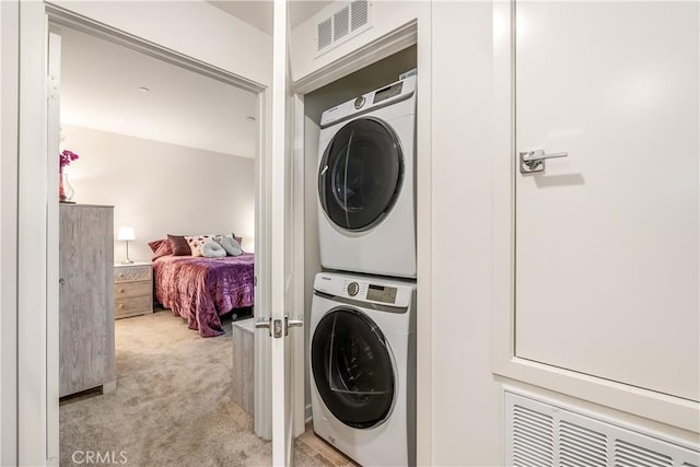 laundry area with stacked washer / drying machine and light carpet