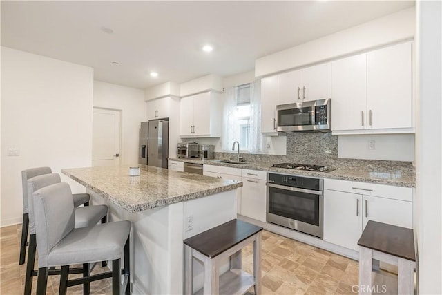 kitchen featuring white cabinetry, appliances with stainless steel finishes, light stone countertops, a breakfast bar, and sink