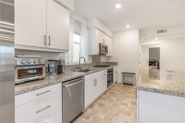 kitchen featuring light stone counters, white cabinets, appliances with stainless steel finishes, and sink