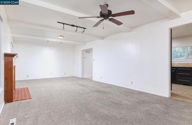 carpeted spare room with ceiling fan, track lighting, a brick fireplace, and beamed ceiling