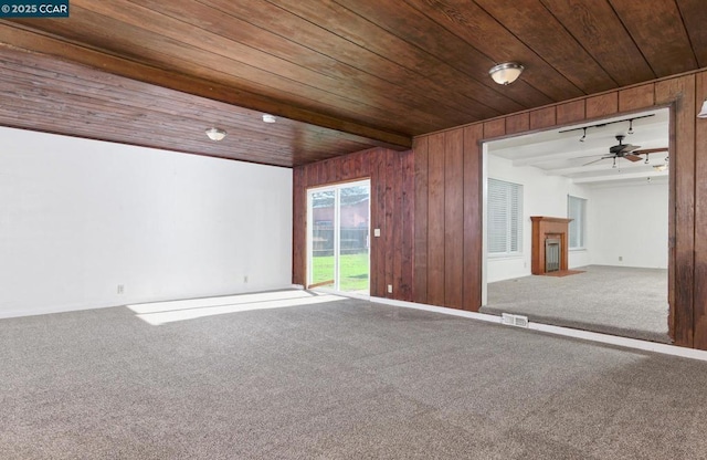 carpeted spare room featuring beam ceiling, ceiling fan, wood walls, and wood ceiling