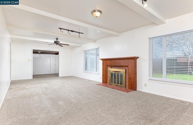 unfurnished living room with track lighting, carpet floors, beamed ceiling, ceiling fan, and a brick fireplace