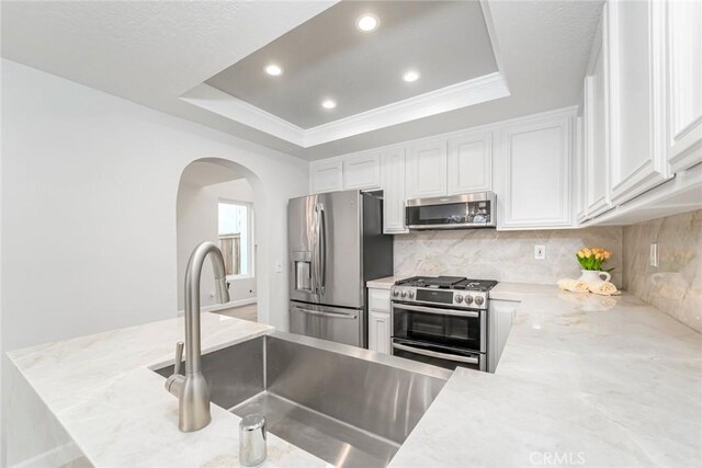 kitchen with a raised ceiling, appliances with stainless steel finishes, and white cabinets