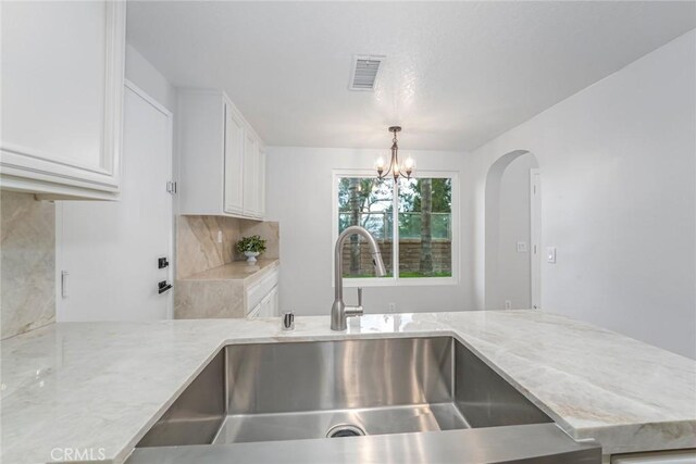 kitchen featuring sink, light stone counters, decorative light fixtures, a notable chandelier, and white cabinets