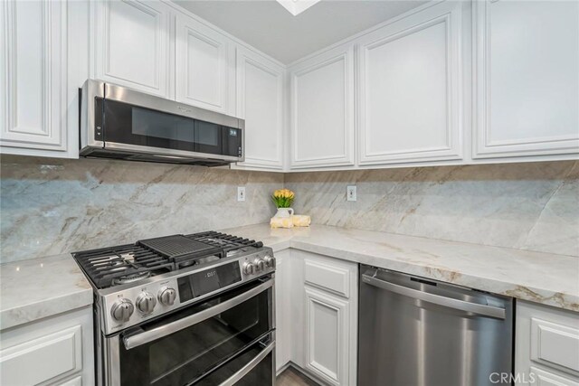 kitchen featuring white cabinetry, appliances with stainless steel finishes, light stone countertops, and backsplash